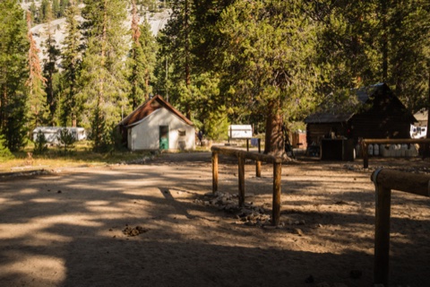 Evening light across the clearing between the camp's outbuildings.