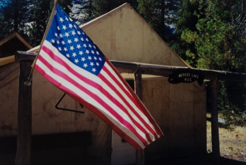 The American flag flying over the Merced Lake H.S.C. sign at the camp entrance.