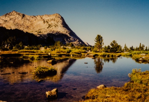 A still tarn on the meadow bench, the ridge mirrored in the water.