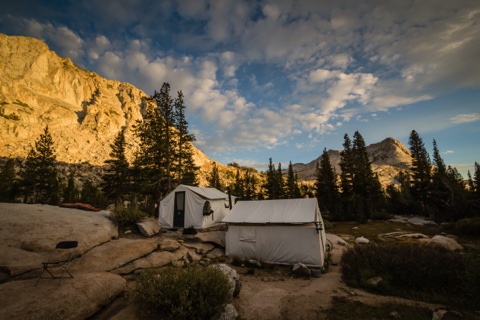 Tent cabins on the granite at golden hour, sunlit wall of the ridge behind.