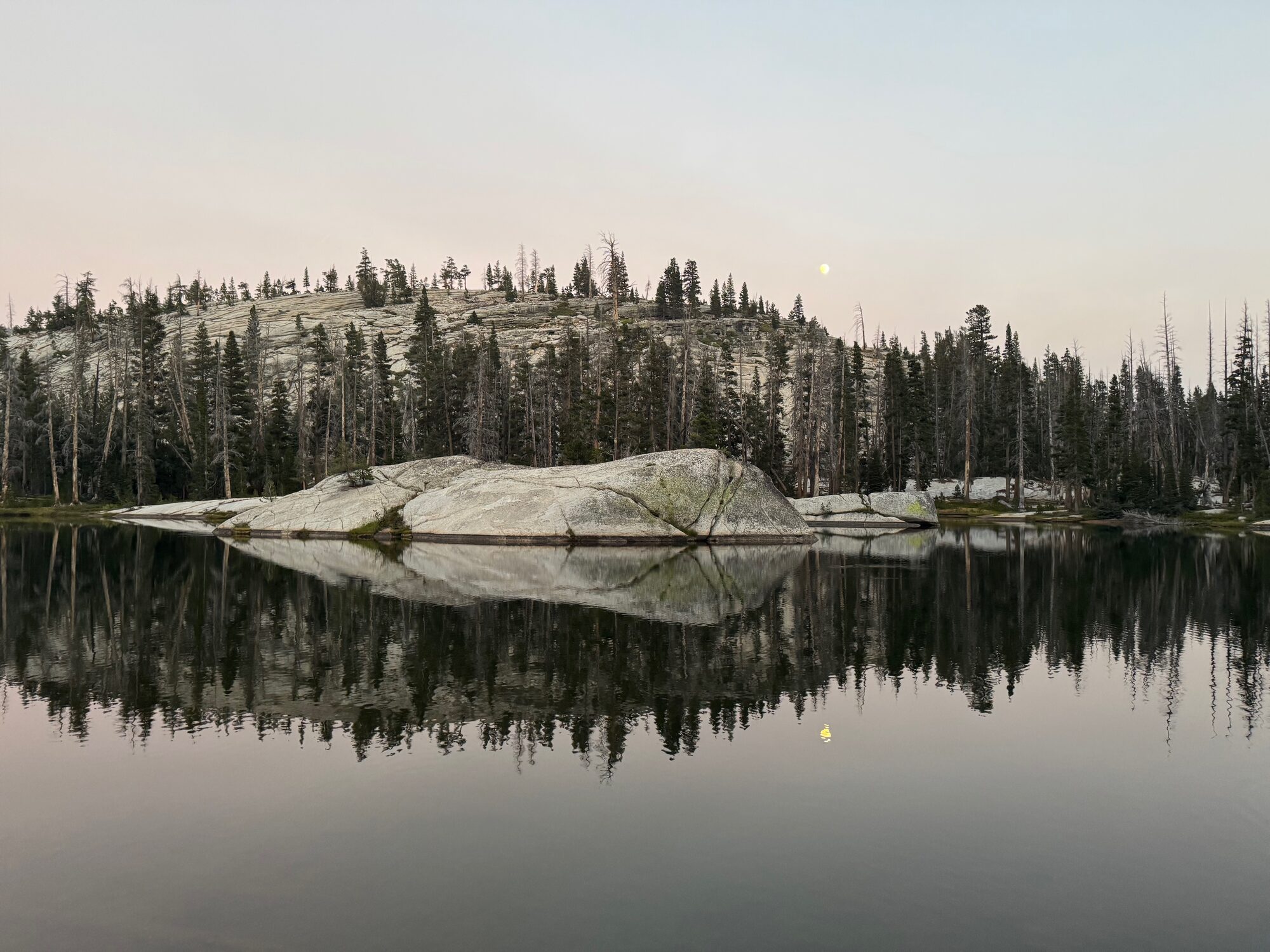 A granite island reflected in a glassy lake at dawn