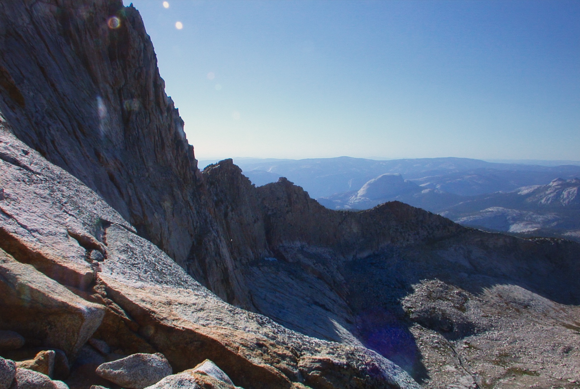 Looking down a granite ridge from high on Mount Clark to Half Dome and Clouds Rest far below